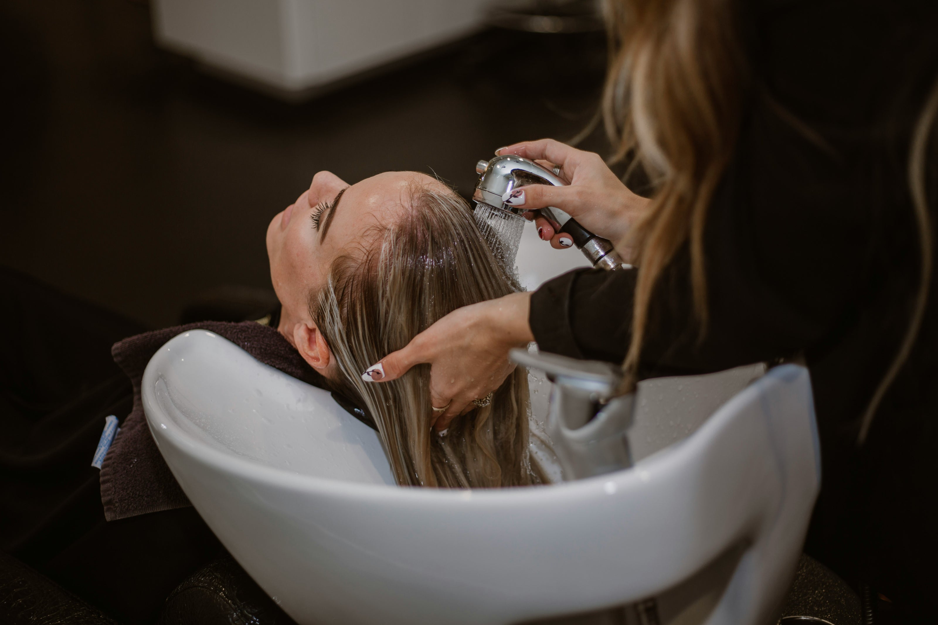 Person getting hair washed in a salon setting with a hairdresser using a spray bottle.